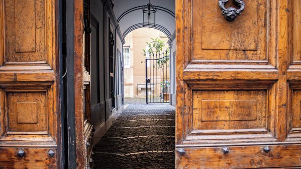 Eine Holztreppe führt zu einem Innenhof mit einem Metallgitter und einer Bank.