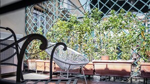 Eine Terrasse mit einem Metallstuhl, Blumentöpfen und einem Metallzaun.