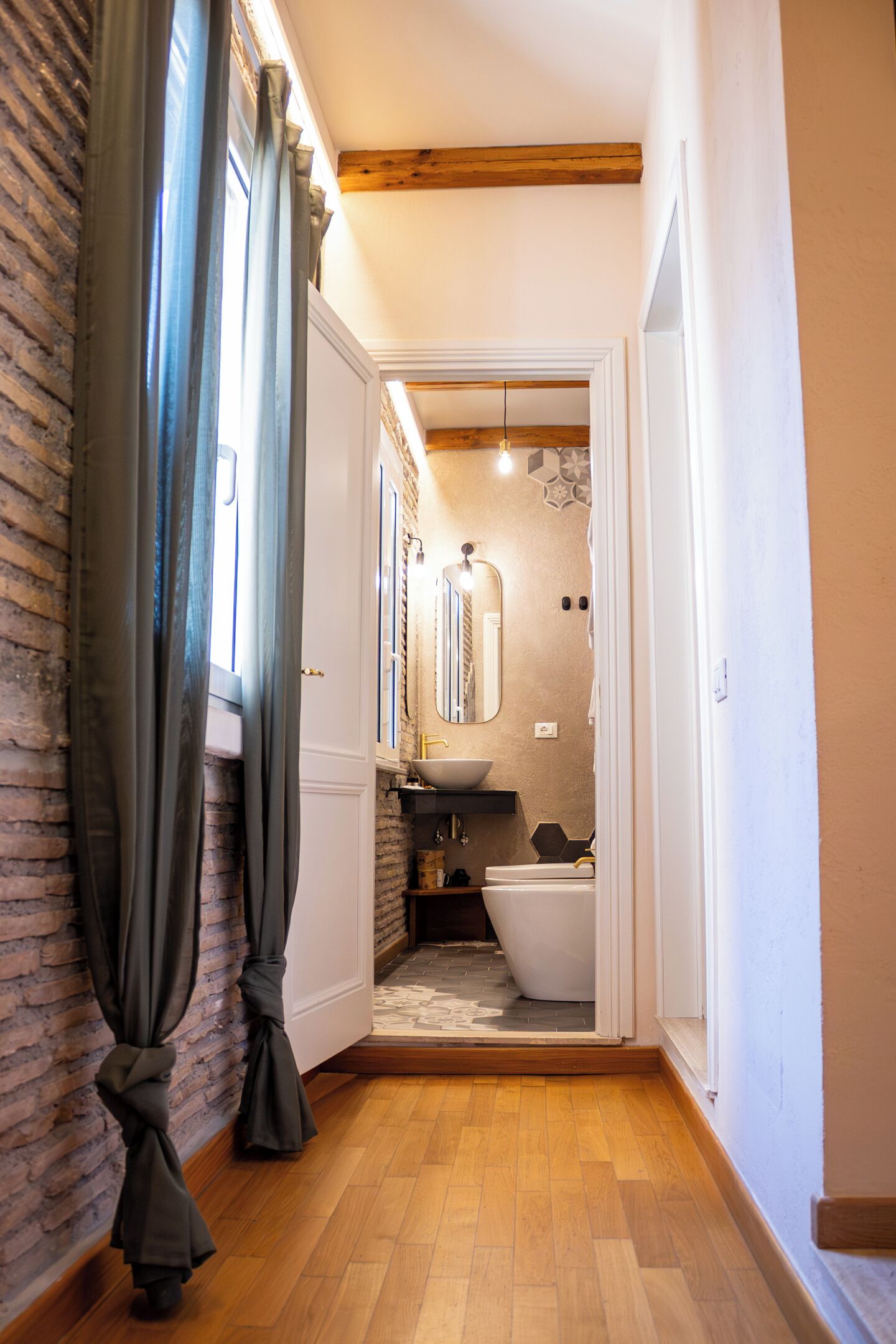 Un corridoio stretto che porta a un bagno con lavandino bianco, uno specchio e un water.