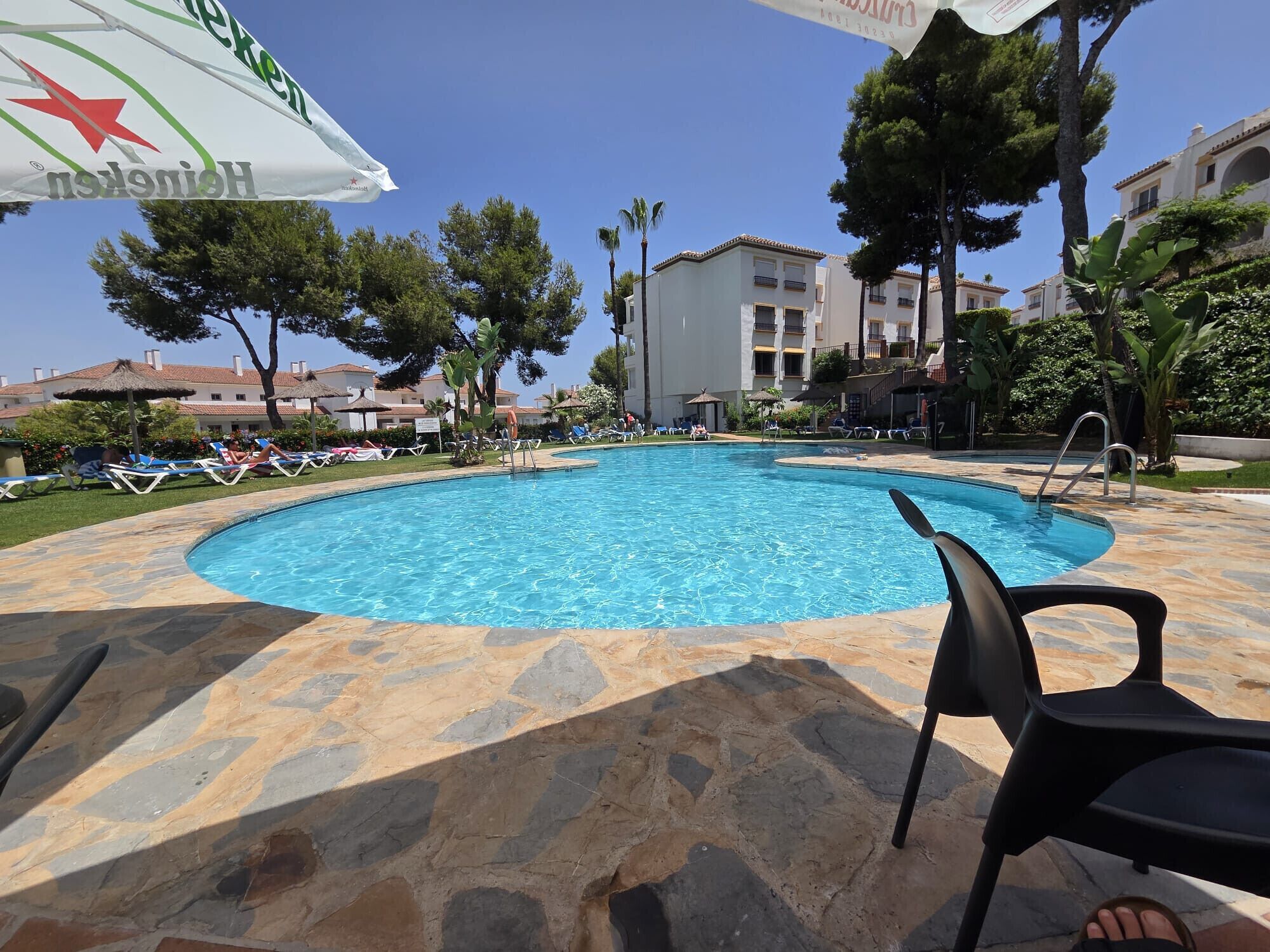 A swimming pool with lounge chairs, a stone deck, and a building in the background.