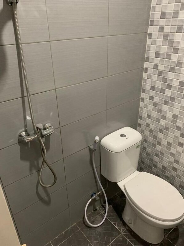 A bathroom with a toilet, a shower, and a tiled wall.