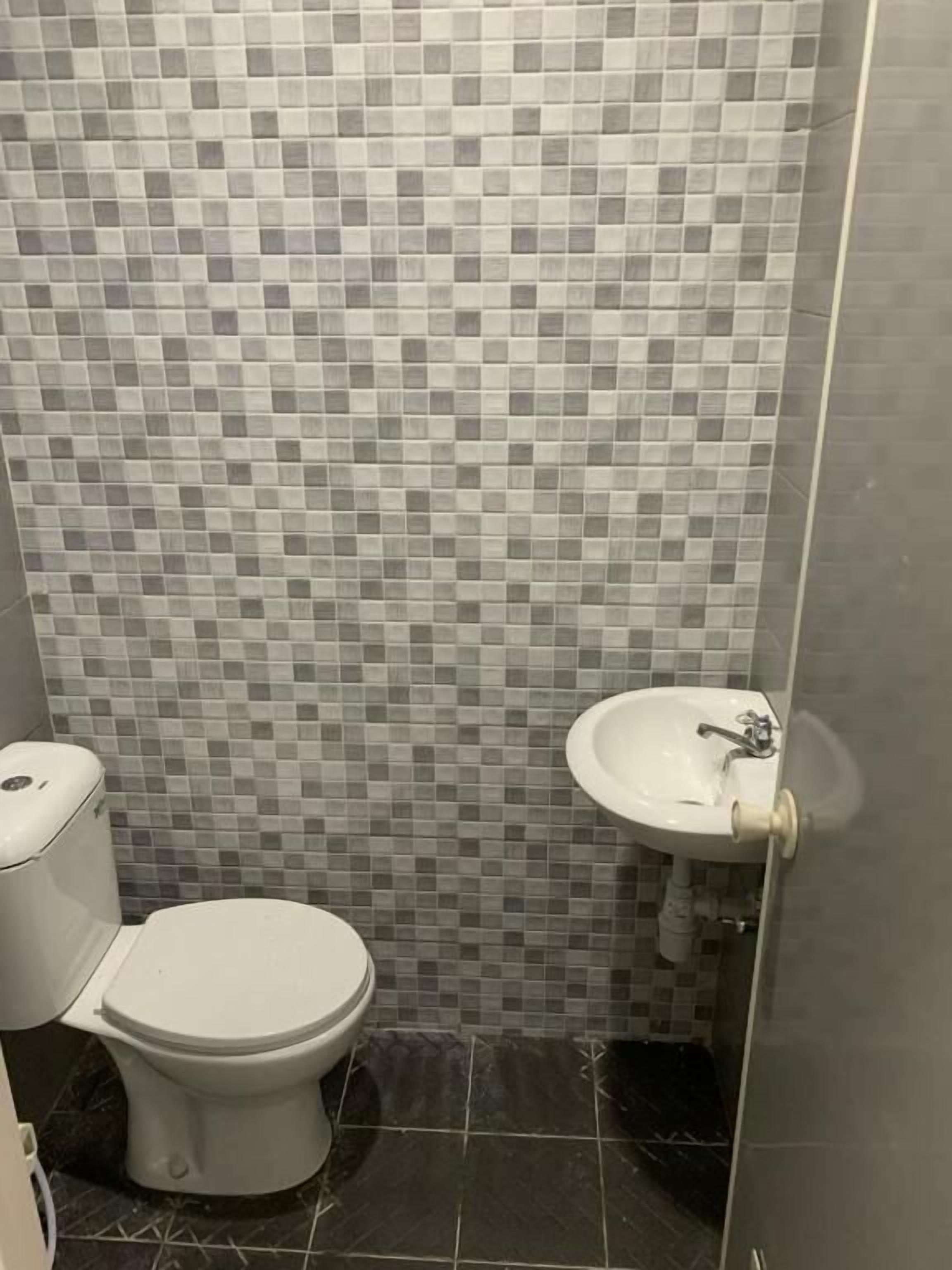 Et badeværelse med fliserede vægge, toilet og håndvask.