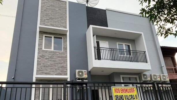 Un edificio moderno con un balcón, un cartel con texto y una valla de metal negro.