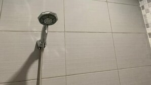 Ducha con cabezal de mano, paredes de azulejos y un respiradero en el techo.