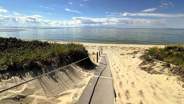 A sandy beach path leading to the ocean with a clear sky.