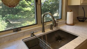 A kitchen with a sink, faucet, and window overlooking greenery.