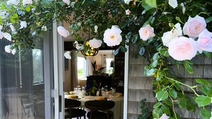 A dining area with a table set for two, a chair, and a plant with pink flowers.
