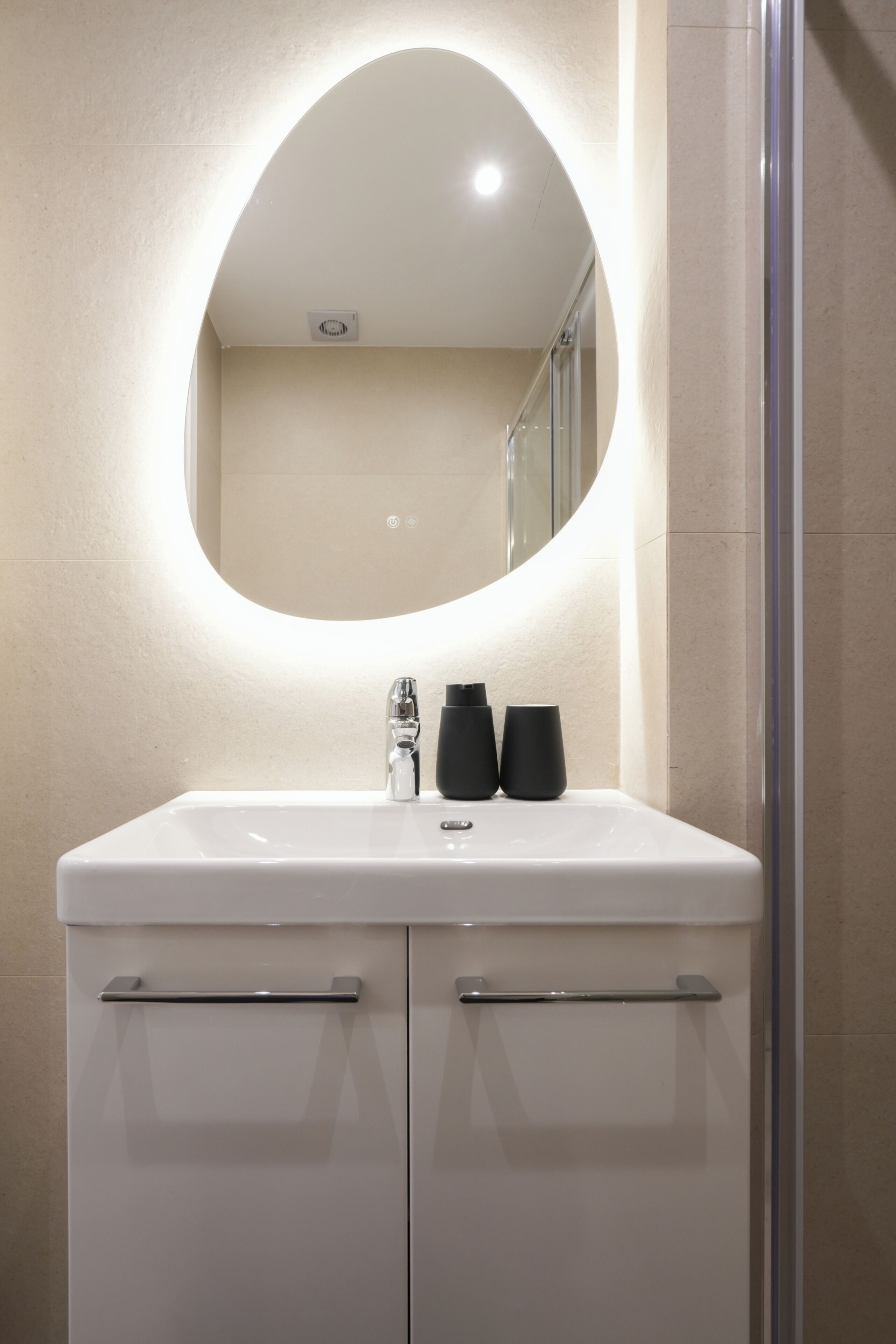 Une salle de bain avec un lavabo blanc, un miroir rond et une cabine de douche en verre.