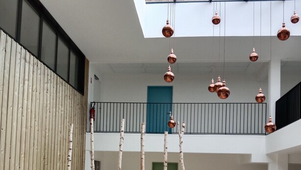 A spacious atrium with a high ceiling, a wooden wall, a central garden area with plants, and a staircase leading to an upper level. - New apartment in a luxury residence on the waterfront of Lake Carcans. (Carcans)