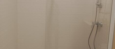 A glass-enclosed shower stall with a handheld showerhead and a wall-mounted faucet.