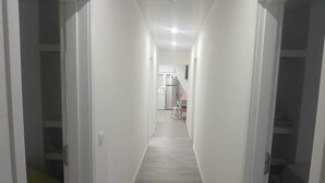 Un pasillo estrecho con paredes blancas y suelo de madera, que conduce a una zona de cocina con un refrigerador y una pequeña mesa.