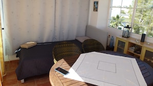 Quarto com cama, mesa, cadeira, janela com vista e cortina estampada.