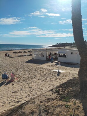A beach with sun loungers, umbrellas, a small kiosk, and a white building with a flat roof. - Costa Blanca vacation rental with ocean views, in a quiet yet central location (Orihuela)