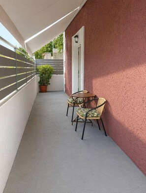 A balcony with a table and chairs, a potted plant, and a door. - Valira Cozy Home w Rustic Charm & Private Garden (Valira)