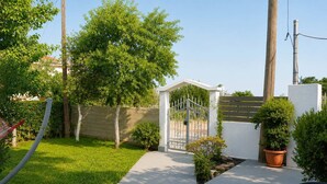 Un giardino con vialetto lastricato, cancello bianco e una piccola costruzione bianca.