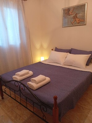 A neatly made bed with patterned bedding, a painting on the wall, and a window with curtains. - Valira Cozy Home w Rustic Charm & Private Garden (Valira)