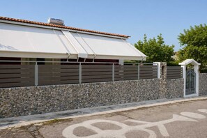 A building with a white awning, a stone wall, and a gated entrance. - Valira Cozy Home w Rustic Charm & Private Garden (Valira)