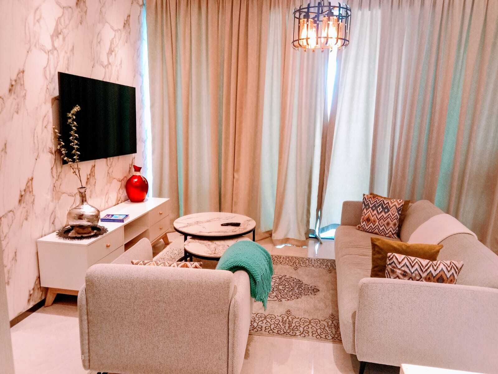 A living room with a sofa, a round coffee table, a TV mounted on the wall, and a decorative vase.
