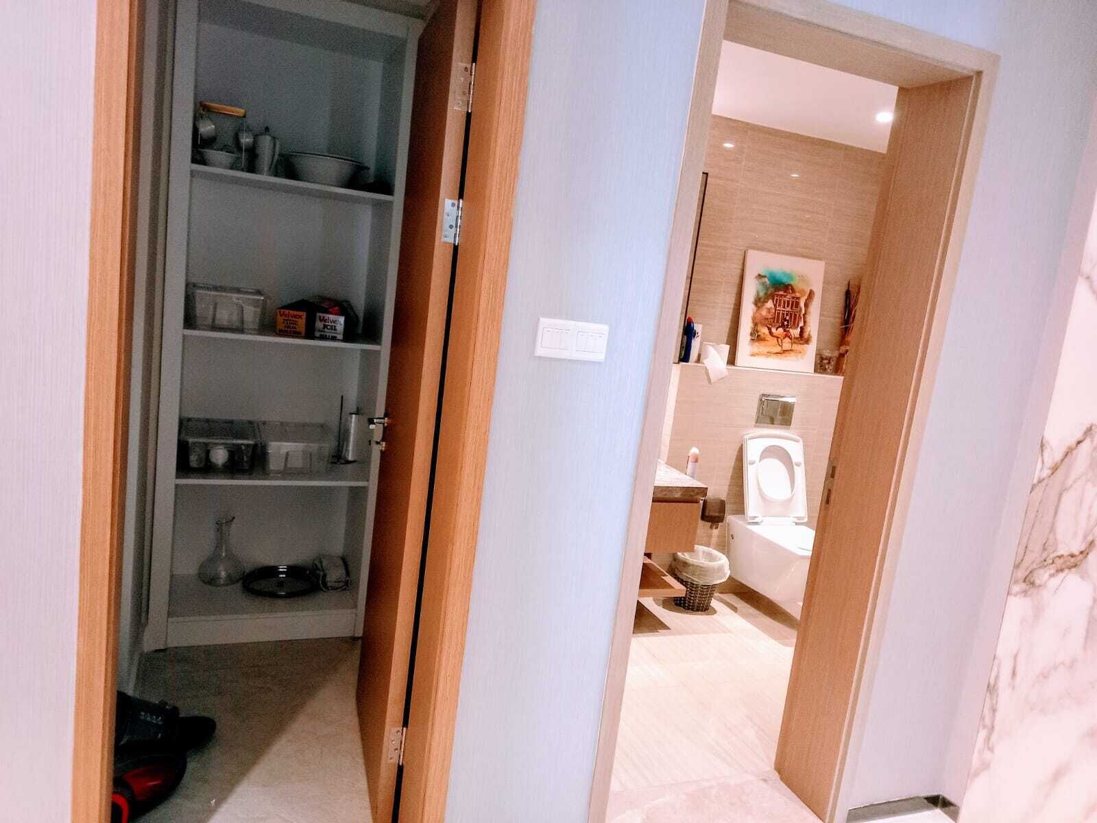 Een gang die leidt naar een badkamer met toilet, wastafel en douche. Er is een plank met diverse spullen en een elektrisch gereedschap op de vloer.