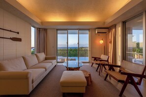 Ein modernes Hotelzimmer mit Sofa, Hocker, Glastisch und Holzstühlen.