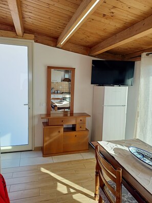 Ein Zimmer mit Holzboden, einem Spiegel, einem Fernseher, einem Kühlschrank, einem Bett und einer Holzkommode.
