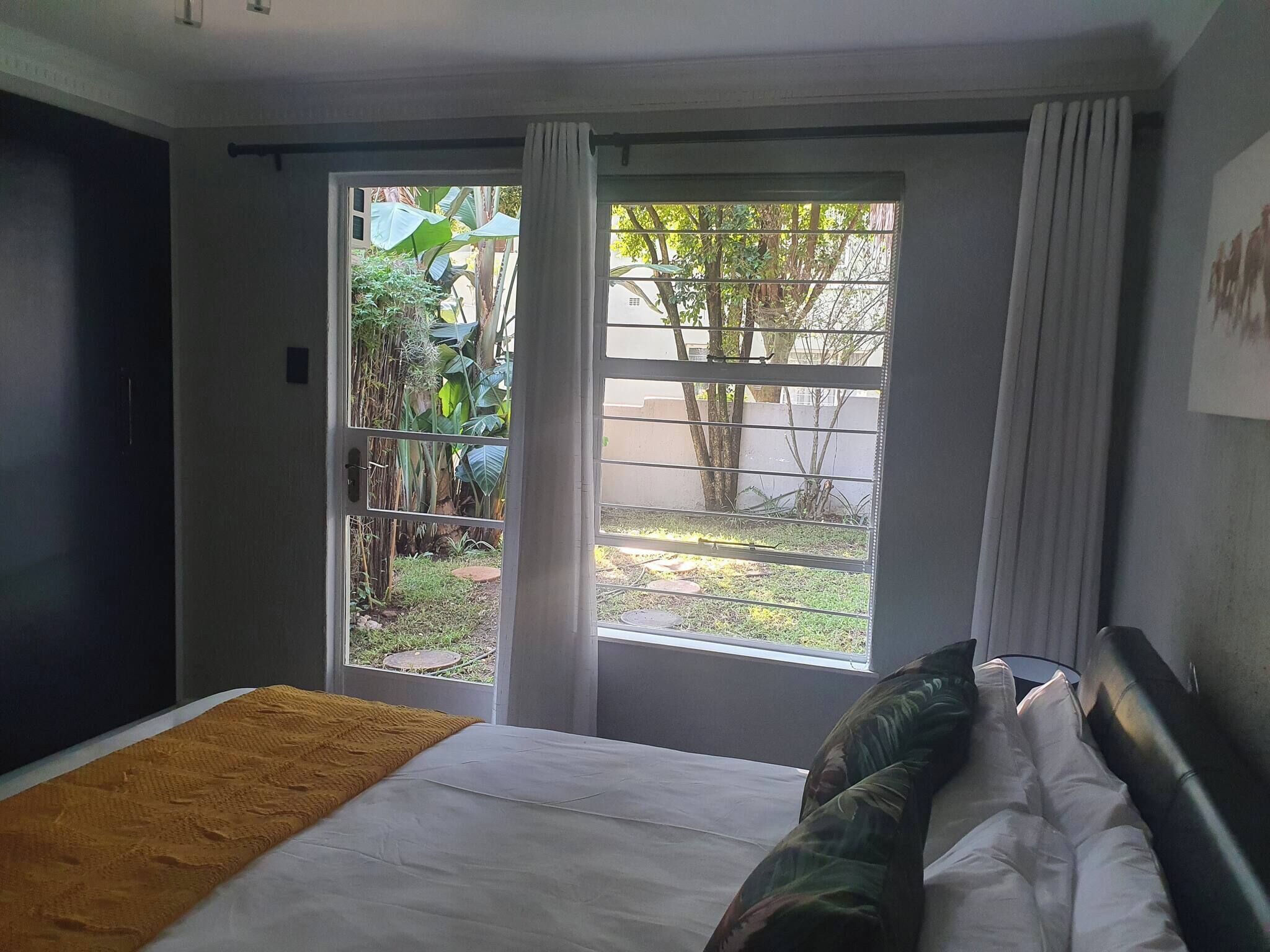 Ein Schlafzimmer mit einem Bett, einem Fenster mit Vorhängen und Blick auf Grünfläche.