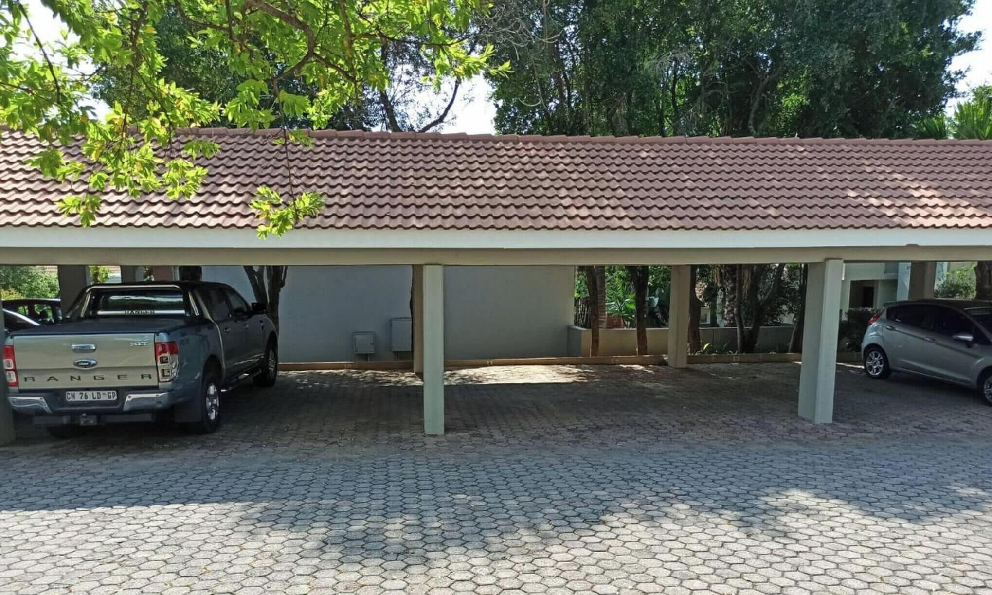 A covered parking area with a tiled roof, two parked vehicles, and a paved ground.