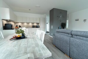 Eine moderne Küche mit weißen Schränken, einem Esstisch mit Blumen in einer Vase und einem grauen Sofa im Wohnbereich.