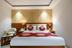 Habitación de hotel con una cama grande, dos mesitas de noche, una silla y cabecera de madera.
