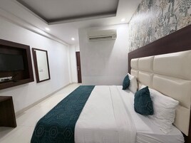 A hotel room with a bed, a television, an air conditioning unit, and a decorative wall.