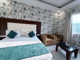 A hotel room with a large bed, a sofa, a small table, and a window with curtains.