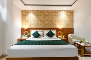 A hotel room with a large bed, two bedside tables, a chair, and a patterned wall.