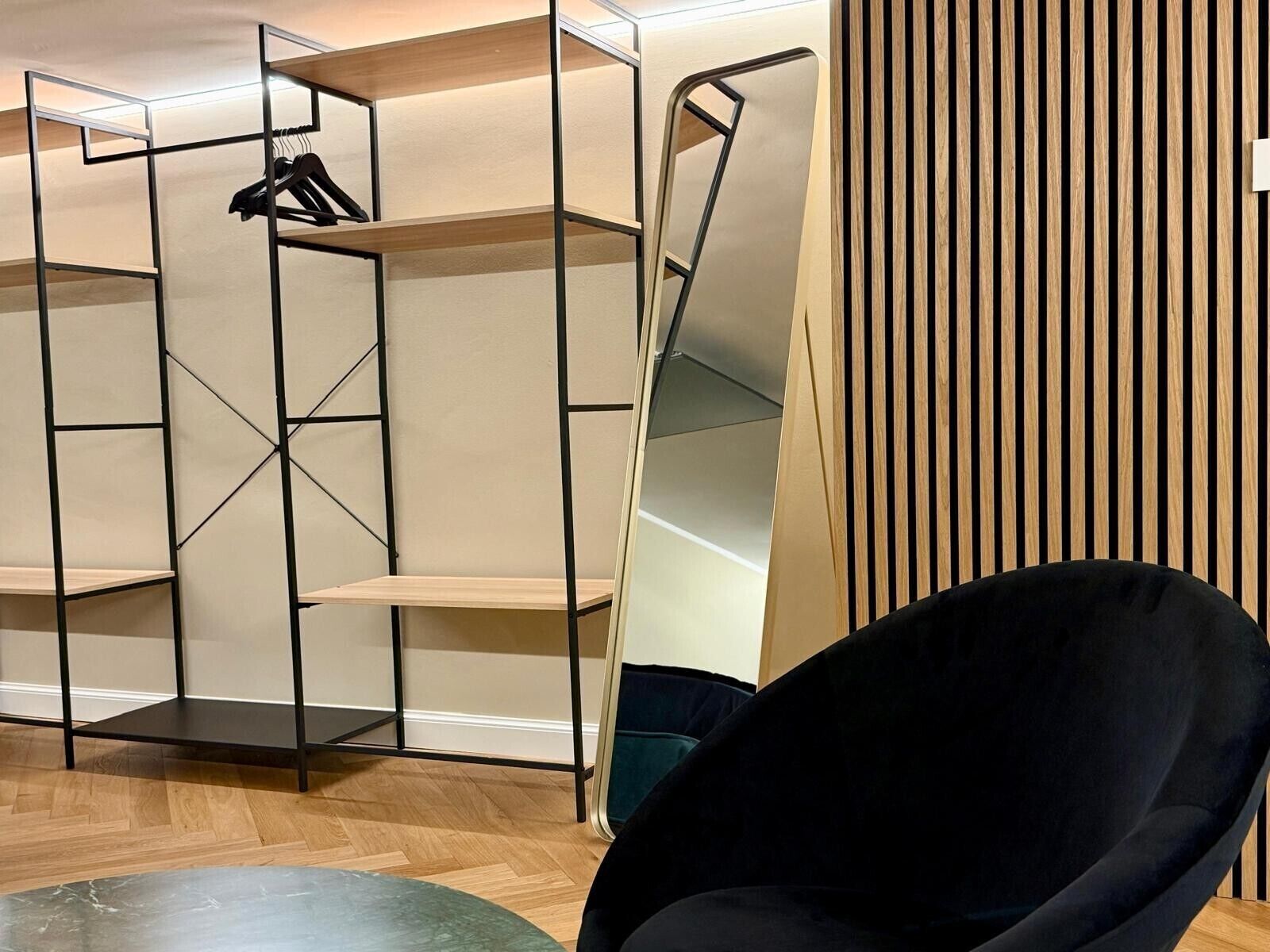 A room with a black chair, a wooden floor, and a metal shelving unit.