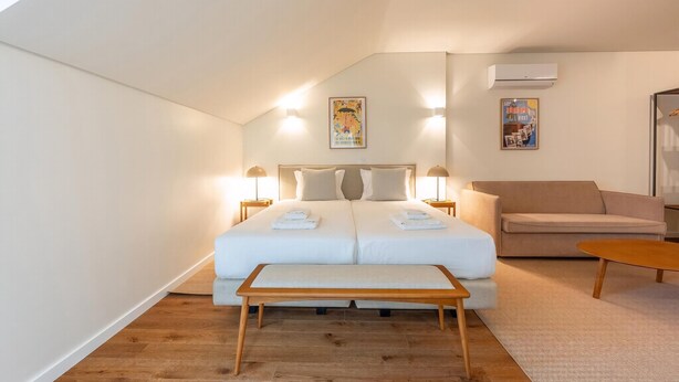 Ein Schlafzimmer mit einem Doppelbett, Nachttischlampen, einer Bank, einem Sofa und zwei Wand-Klimaanlagen.