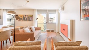 Ein modernes Wohnzimmer mit einer Couch, Sesseln, einem Esstisch und einem Fernseher.