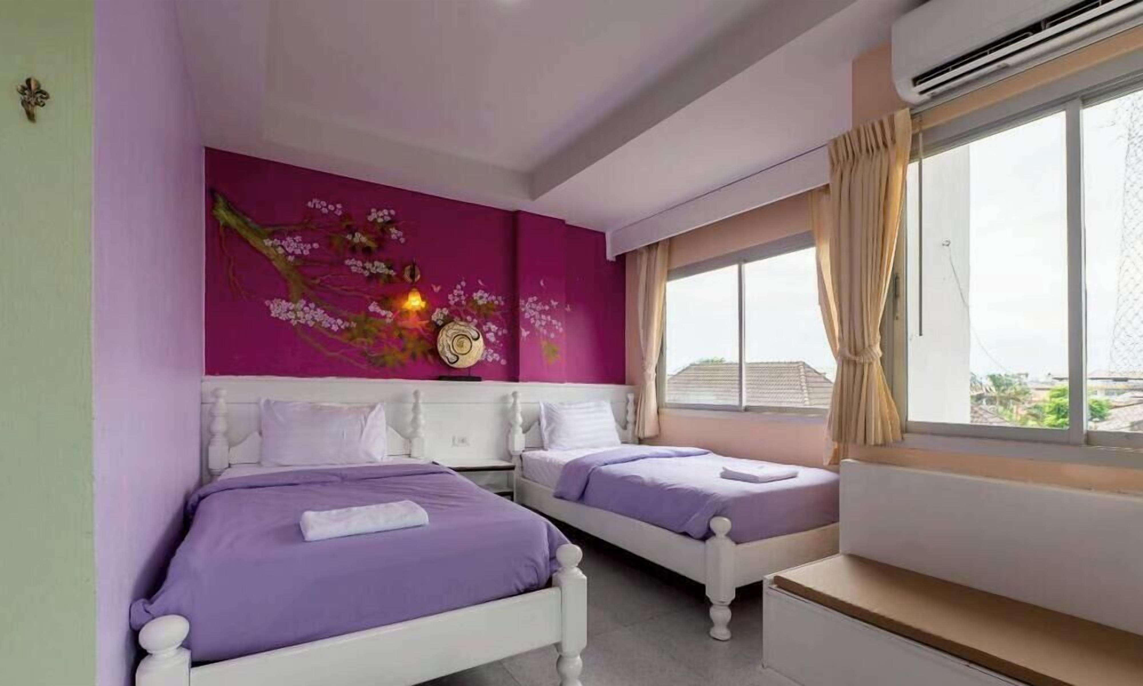Un dormitorio con dos camas, un ventanal grande y una pared con un cuadro floral.