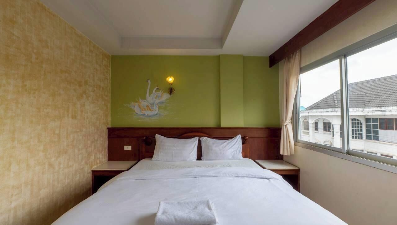 Habitación de hotel con una cama grande, una pared verde, un cuadro de cisnes y una ventana con vistas a edificios.