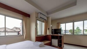 A hotel room with a bed, a TV, a mini-fridge, and large windows.