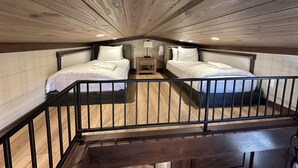 A bedroom with two beds, a nightstand, a lamp, and a wooden ceiling. - Cypress Cabin - Spacious floor plan with modern look, full kitchen, separate bedroom, and upstairs loft (Bellemont)
