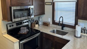 A kitchen with a built-in microwave, stove, oven, and sink. There is a window with blinds, a chandelier, and wooden cabinetry. - Cypress Cabin - Spacious floor plan with modern look, full kitchen, separate bedroom, and upstairs loft (Bellemont)