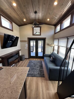 Un intérieur chaleureux avec un plafond en bois, un téléviseur à écran plat fixé au mur, un canapé, une table basse et un escalier.
