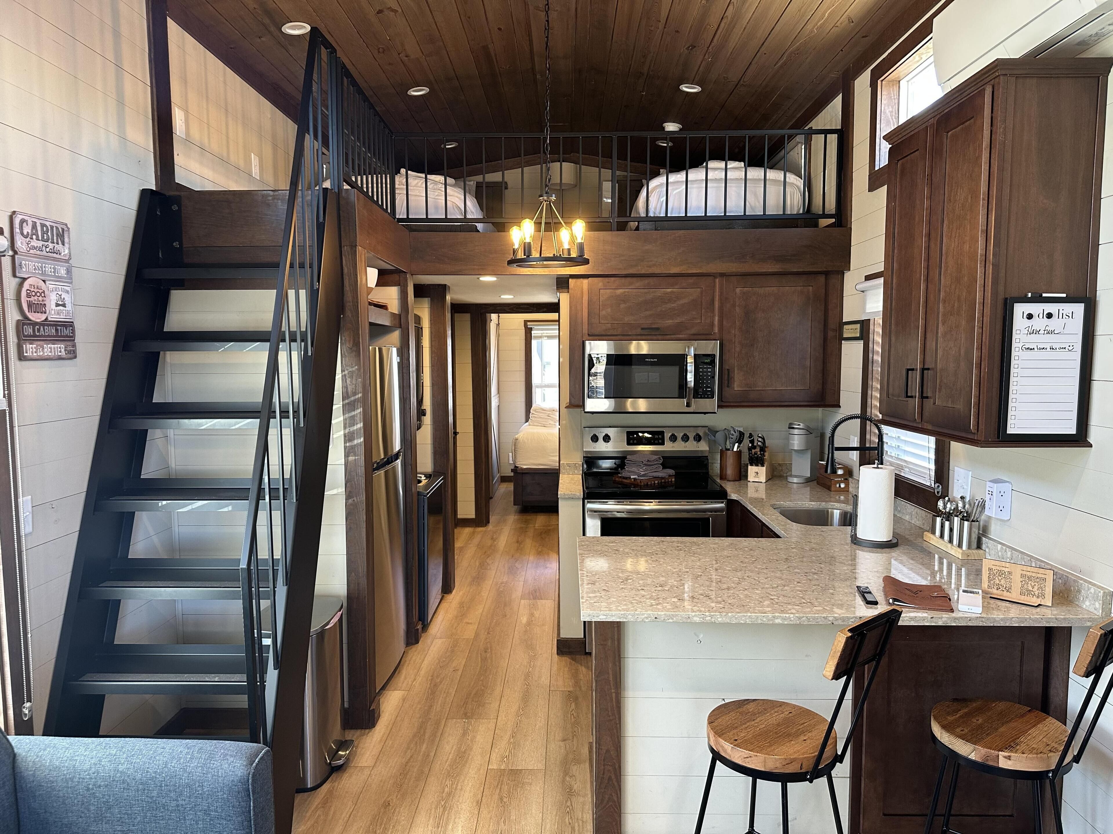 A cabin interior with a kitchen, dining area, and a loft bedroom.