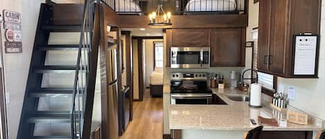 A cabin interior with a kitchen, dining area, and a loft bedroom.