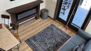 A living room with a TV, fireplace, sofa, dining table, chairs, and a patterned rug. - Cypress Cabin - Spacious floor plan with modern look, full kitchen, separate bedroom, and upstairs loft (Bellemont)