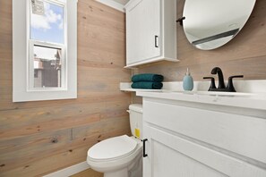 Une salle de bain avec un mur en bois, des toilettes blanches, un lavabo blanc avec un robinet noir et un miroir au-dessus du lavabo.