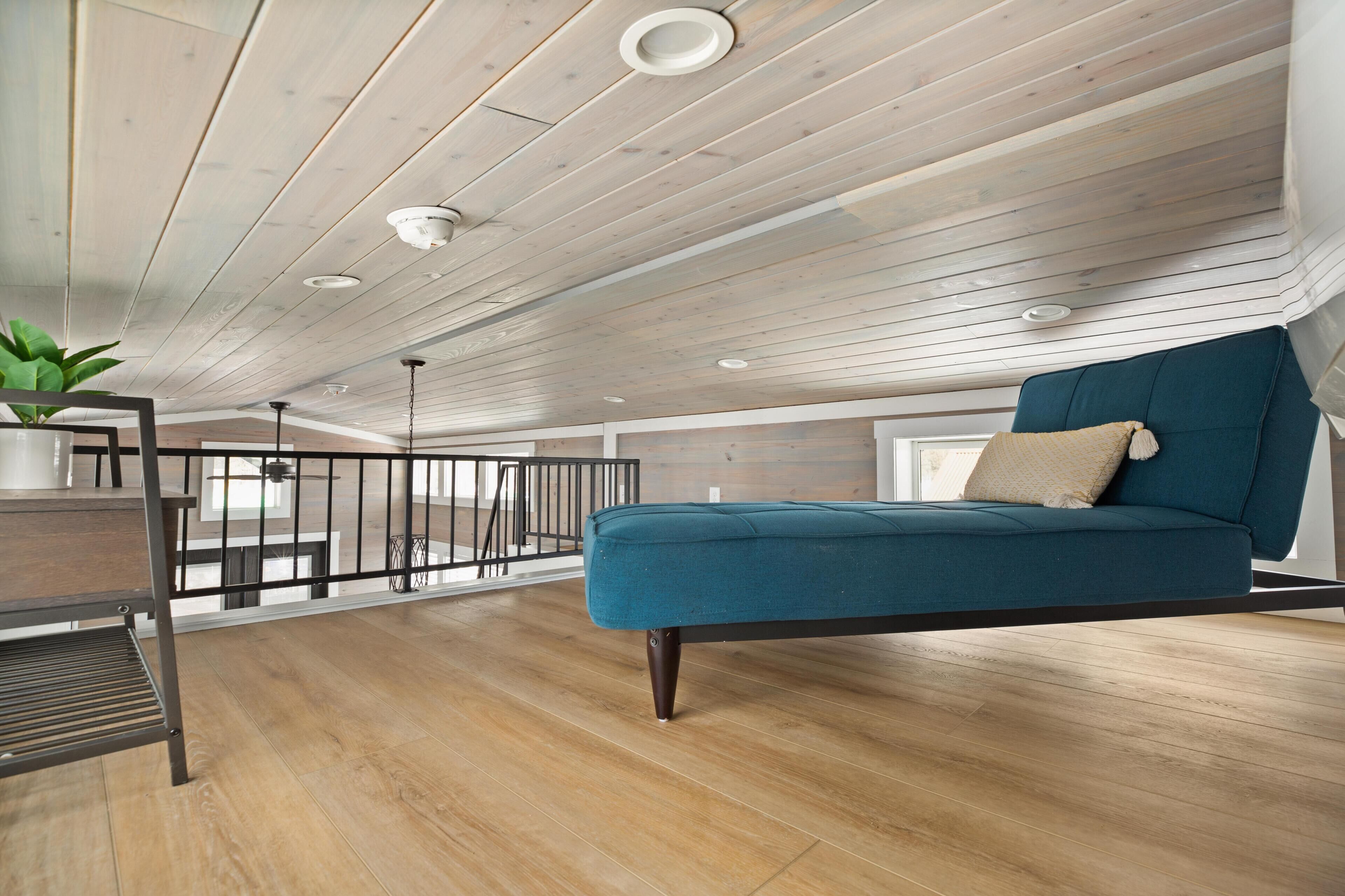 Um quarto moderno estilo loft, com sofá verde-água, piso de madeira e teto com iluminação embutida.