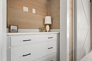 Une commode blanche avec des poignées noires, une horloge murale, un tableau encadré et une lampe.