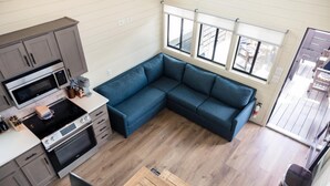 Una cucina moderna con forno integrato e microonde, un divano ad angolo blu e un'ampia finestra con persiane.