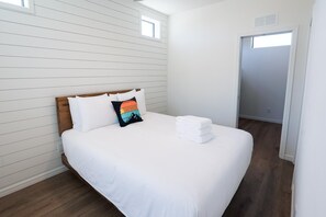 Uma cama bem arrumada com lençóis brancos, cabeceira de madeira e um único travesseiro decorativo.