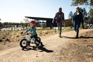 A dirt path with a child on a bicycle, an adult walking, and a building in the background. - Birch Cabin | Roof Top Deck - Birch Cabin 3 bdrm Roof Top Deck (Bellemont)